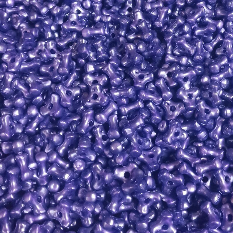 A close-up, top-down view of a dense pile of small, glossy, dark purple pearlized tri beads with 2mm holes, filling the entire frame.