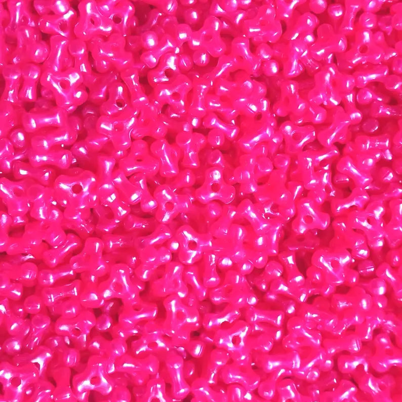 A close-up, top-down view of numerous small, glossy, bright hot pink pearl plastic beads densely packed together.