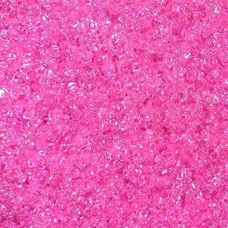 A close-up texture shot of transparent bright pink tri beads densely packed together.